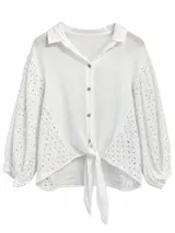Camisa blanca de mangas largas abullonadas, confeccionada en tejido con detalles bordados tipo broderie en las mangas y laterales, cuello camisero, cierre frontal de botones y nudo ajustable en el frente.