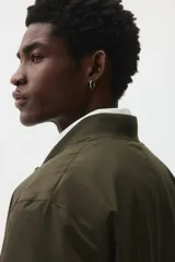 Campera bomber de color verde militar, con cuello elevado acanalado, cierre frontal, bolsillos laterales con cierre y ribetes acanalados en puños y bajo.