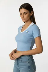 Remera de algodón al cuerpo, con cuello en V y cuello tipo polo en color blanco. Presenta un estampado pequeño de la bandera argentina en el pecho.