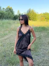 Vestido corto tipo lencero de seda color blanco, con detalles de encaje negro en el escote en V y en el ruedo asimétrico. Presenta breteles finos ajustables y una caída fluida.