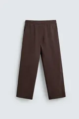 Pantalón jogger de algodón color marrón oscuro, de corte relajado y pierna ancha. Presenta cintura elástica con cordón ajustable y bolsillos laterales y uno trasero de plastrón.