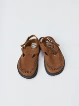 Slipper tipo guillermina confeccionada en gamuza color marrón, con plataforma de goma negra y doble hebilla ajustable. Presenta un pespunte decorativo en el borde inferior y cuenta con interior recubierto en cuero.