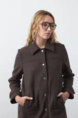 Tapado corto de paño color marrón, con diseño recto, cuello camisero y cierre frontal con broches metálicos. Cuenta con bolsillos frontales.