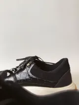 Zapatillas deportivas negras de cuero, con cordones y suela de goma blanca con base marrón.