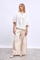 Blusa blanca de lino con cuello mao, mangas 3/4 abullonadas con apliques bordados en forma de hojas y cierre frontal con botones.