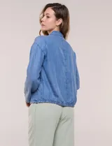Camperita de denim liviano color azul, con cuello camisero, botones frontales ocultos, mangas largas de hombros caídos, bolsillos laterales y cordón ajustable en la cintura.