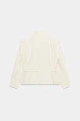 Blazer corto de color marfil con cuello subido, manga larga y bolsillos laterales. Cuenta con un cinturón del mismo tejido para anudar en la cintura, forro interior a tono y cierre frontal con cremallera y botones a presión ocultos bajo solapa.