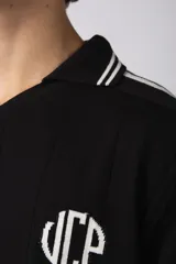 Remera tipo chomba de tejido de punto color blanco, con cuello en V y mangas cortas. Presenta rayas verticales sutiles en la trama y estampado gráfico frontal con la inscripción CNPT STUDIO y detalles en negro.