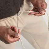Pantalón de jogging Adidas de corte regular en color beige, con las tres tiras características en negro a lo largo de los laterales y el logo del trifolio bordado en la parte frontal.