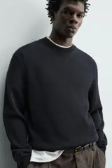 Sweater de punto negro de corte regular fit, confeccionado en algodón con cuello redondo, manga larga y acabados en rib.