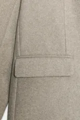 Blazer de corte recto y diseño minimalista, confeccionado en tejido de paño suave color beige. Presenta cuello con solapas clásicas, cierre frontal con un solo botón y dos bolsillos delanteros con solapa.