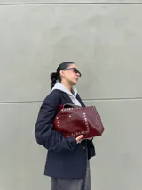 Cartera de cuero color bordeaux con tachas plateadas, cierre con pastillas imantadas, sobre interno grande enganchado y bolsillo externo con pastilla imantada.