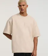 Remera oversize color beige de gamuza sintética, con cuello redondo, manga corta y bordado de cruz en el centro del frente.