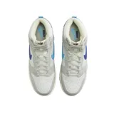 Championes Nike Dunk High Retro SE de corte alto, con diseño en paneles de cuero blanco y gris. Presenta un swoosh lateral dividido en dos tonos de azul, suela intermedia con acabado envejecido y suela exterior bicolor en azul claro y oscuro.