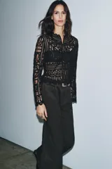 Blusa negra de manga larga confeccionada en tejido tipo crochet con intrincados patrones geométricos y florales. Presenta cuello redondo y cierre frontal con botones.