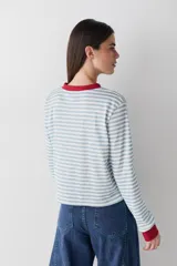 Remera de manga larga con diseño de rayas horizontales en color celeste y blanco. Presenta cuello redondo y puños en color rojo contrastante, junto con un pequeño parche bordado en el pecho.