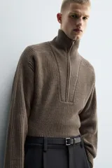 Jersey de punto de corte relajado, color marrón, con cuello perkins y cierre frontal de cremallera. Presenta manga larga y acabados en rib en puños y bajo.