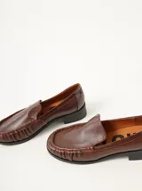 Mocasines de cuero negro con costuras pespunteadas en hilo blanco a contraste, diseño fruncido en la puntera, talón plano con pequeño tacón y apliques sutiles en charol.