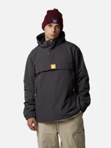 Canguro tipo anorak de color gris oscuro, con capucha ajustable, bolsillo frontal con solapa y cierre de media cremallera. Presenta detalles en color naranja en los tiradores de los cierres y un parche con el logo de la marca en el centro del pecho.