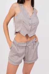 Short de vestir color gris con finas rayas verticales blancas, tiro alto, pinzas delanteras, bolsillos laterales y ruedo con dobladillo. Cierre frontal con botón y cremallera.