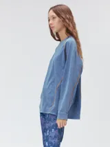 Remera de manga larga MUTMA Sticha, color negro con efecto acid wash y costuras decorativas expuestas en color celeste brillante. Cuenta con corte clásico, cuello redondo a la base y calce holgado.