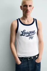 Camiseta sin mangas slim fit color blanco, con cuello redondo y sisas ribeteadas en azul marino. Estampado frontal con la palabra "League" y el número "'86" en azul marino.