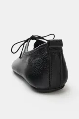 Zapato plano tipo bailarina confeccionado en piel con textura granulada. Presenta cierre mediante lazo en la parte delantera, punta redonda y tirador en la parte trasera.