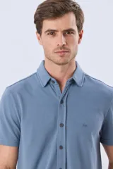 Camisa de piqué lisa color celeste, de manga corta, con cuello camisero y cierre frontal de botones oscuros.
