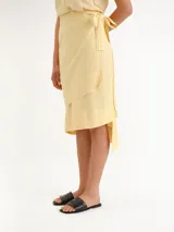 Pollera midi color amarillo claro, tipo envolvente (wrap), con diseño asimétrico en capas y lazo lateral para anudar.