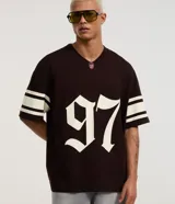 Remera de algodón marrón oscuro con cuello en V, manga corta y corte overboxy. Presenta diseño deportivo de fútbol americano con el número "97" estampado en gran tamaño en el frente y franjas blancas en las mangas.