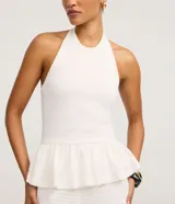 Top blanco de tejido piquet texturizado, con cuello halter y peplum con volado en la cintura.