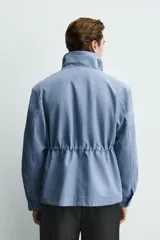 Cazadora de algodón lavado en color azul, corte regular fit, con cuello subido, bolsillos frontales de plastrón con solapa y cierre frontal de cremallera oculta con solapa de botones a presión.