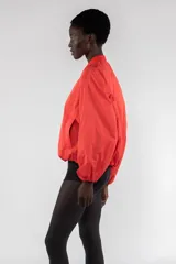 Campera bomber color rojo anaranjado de nailon repelente al agua, corte regular, cierre frontal con cremallera visible, tirador con logo bordado, bolsillos de ribete verticales, hombro caído, bolsillo utilitario con cremallera en la manga, cuello de chaqueta bomber acanalado y puños y bajo elásticos fruncidos.