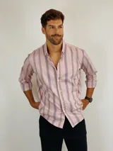 Camisa de manga larga con estampado de rayas verticales en tonos rosados y violetas. Presenta cuello clásico, cierre frontal con botones y un pequeño logo bordado en el pecho.