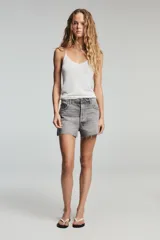 Shorts de denim gris claro con efecto lavado, tiro bajo y corte ancho (baggy). Presenta cinco bolsillos y cierre frontal con cremallera y botón metálico.