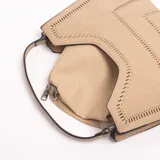 Cartera Xavielle de diseño estructurado trapezoidal en color beige, confeccionada en material sintético con efecto gamuza. Presenta detalles de perforaciones geométricas en los bordes y el centro, con un asa corta superior y cierre principal.