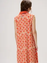 Vestido midi camisero sin mangas, de corte recto y holgado. Cuenta con cuello camisero liso en color naranja y cierre frontal parcial con botones. Presenta un estampado geométrico psicodélico en tonos naranja y beige.