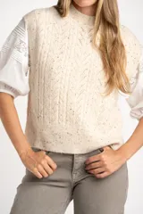 Chaleco de tejido de punto color beige melange con textura tweed y cuello redondo. Presenta un patrón de rombos calados y trenzas.