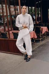 Pantalón jogger de felpa color gris claro melange, de tiro medio con cintura elástica. Presenta detalles de aplicaciones tejidas a contraste en los laterales y terminaciones con puños abullonados.