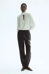 Blusa de gasa color beige con estampado de lunares negros, cuello alto con moña integrada y mangas largas abullonadas con puños ajustados.