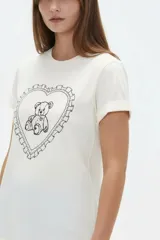 Remera de algodón color beige, de manga corta con vuelta, cuello redondo y estampa frontal de flores con lazo en tonos azules y celestes.
