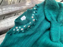 Sweater tejido a mano de lana merino color verde oscuro, con cuello alto, mangas abullonadas y detalle de bordado floral artesanal en el canesú.