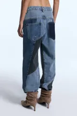 Pantalón de jean con diseño de patchwork que combina diferentes tonos de denim en paneles geométricos. Presenta un corte relajado, tiro medio y cierre frontal con botón metálico.