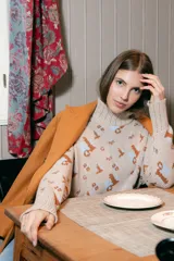 Polera de tejido de punto con cuello alto, diseño holgado y estampado jacquard con motivos geométricos y figuras en tonos beige, naranja y celeste.