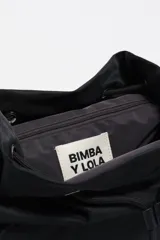 Mochila mediana de nylon negro con estructura blanda, cierre de solapa con mosquetón y cordón ajustable. Cuenta con bolsillos laterales con cierre, asa superior y logo metálico de la marca en el frente.