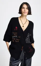 Cardigan negro de punto con escote en V y cierre frontal de botones. Presenta mangas tres cuartos y bolsillos frontales. El diseño destaca por sus bordados coloridos con motivos de cerezas y frases en francés distribuidas por toda la prenda.