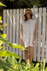 Vestido corto de algodón color blanco, con diseño holgado, cuello redondo y mangas cortas. Presenta detalles de bordados florales en los laterales.