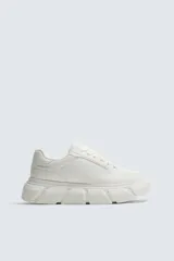 Zapatilla urbana de color blanco con diseño de suela gruesa con volumen y textura irregular. Presenta un corte superior con paneles combinados y cierre mediante cordones al tono.