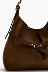 Cartera tipo hobo de diseño slouchy, color marrón, con correa de hombro ajustable y detalle de tira fina frontal con cierre de mosquetón metálico.