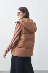 Chaleco puffer negro con diseño acolchado, capucha desmontable y cierre frontal. Cuenta con cordones ajustables en la cintura y bolsillos laterales.